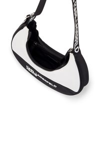 Juoda ir balta rankinė su apvaliu dizainu, blizgia medžiaga, užtrauktuko uždarymu ir iškilniu logotipu priekyje. Įtraukta reguliuojama rankena.