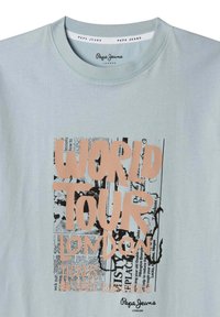 Světle modré bavlněné tričko s vícebarevným textem. Design obsahuje "SVĚTOVÉ TURNÉ", "LONDÝN" a grafické prvky v černých a korálových tónech.