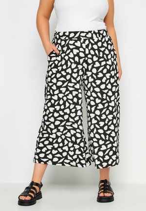 Black culottes with a white heart pattern, elastic waistband, side pockets, and a relaxed fit. Paired with black strappy sandals.