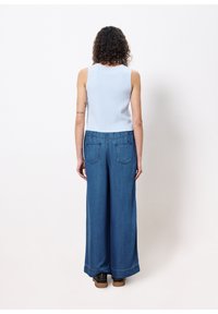 Un haut sans manches en maille bleu clair associé à un pantalon en denim bleu à jambes larges. Le pantalon présente des poches arrière et un ourlet qui s'évasent légèrement.