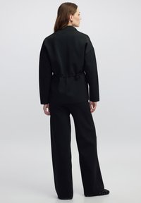 Zwarte relaxte outfit bestaande uit een lange mouw top met een tailleband en wijde broek, gemaakt van een gladde, gestructureerde stof.