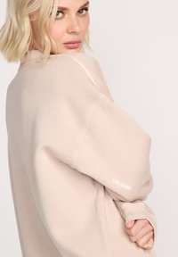Jasnoróżowy, oversize'owy sweatshirt o miękkiej fakturze, z prążkowanym dekoltem typu crew i opadającymi ramionami. Na rękawie znajduje się logo "VOLCOM".