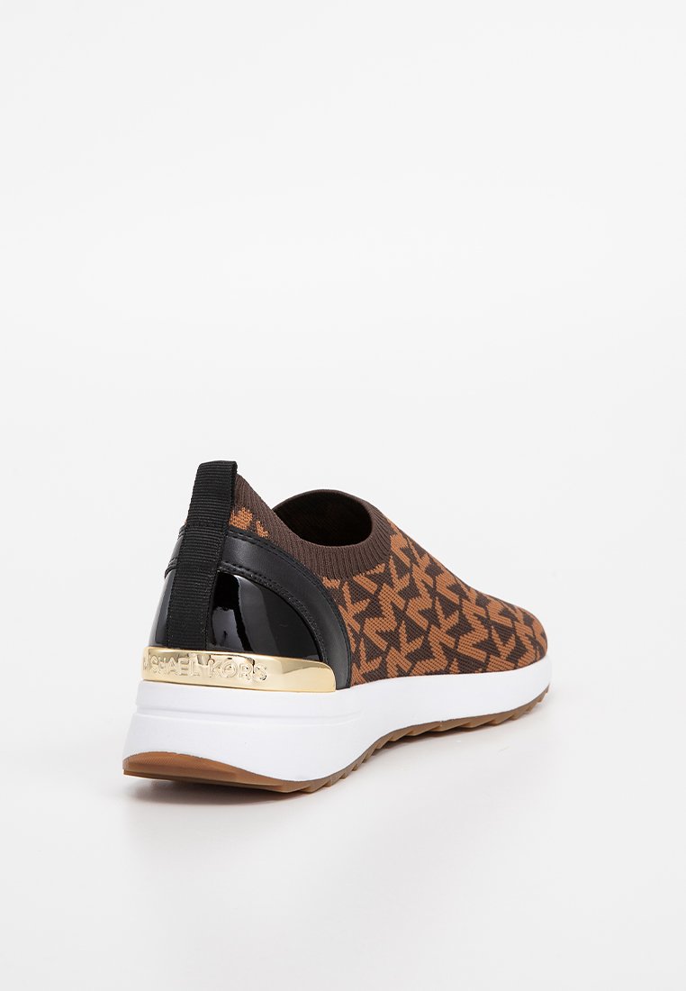 Braune Slip-On-Sneaker mit schwarzem Lackabsatz, goldener Michael Kors Logo-Plakette, gestricktem Obermaterial mit Monogramm-Muster und weißer Sohle.