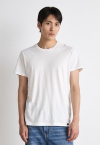 Hvit bomulls T-skjorte med rund hals og korte ermer, avslappet passform med subtil tekstur. Kombinert med lyseblå denimjeans.