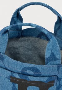 Τσάντα ώμου από μπλε τζιν με δύο λαβές και μαύρο τυπωμένο σχέδιο στην μπροστινή τσέπη, εμφανιζόμενη ανοιχτή από ψηλά.