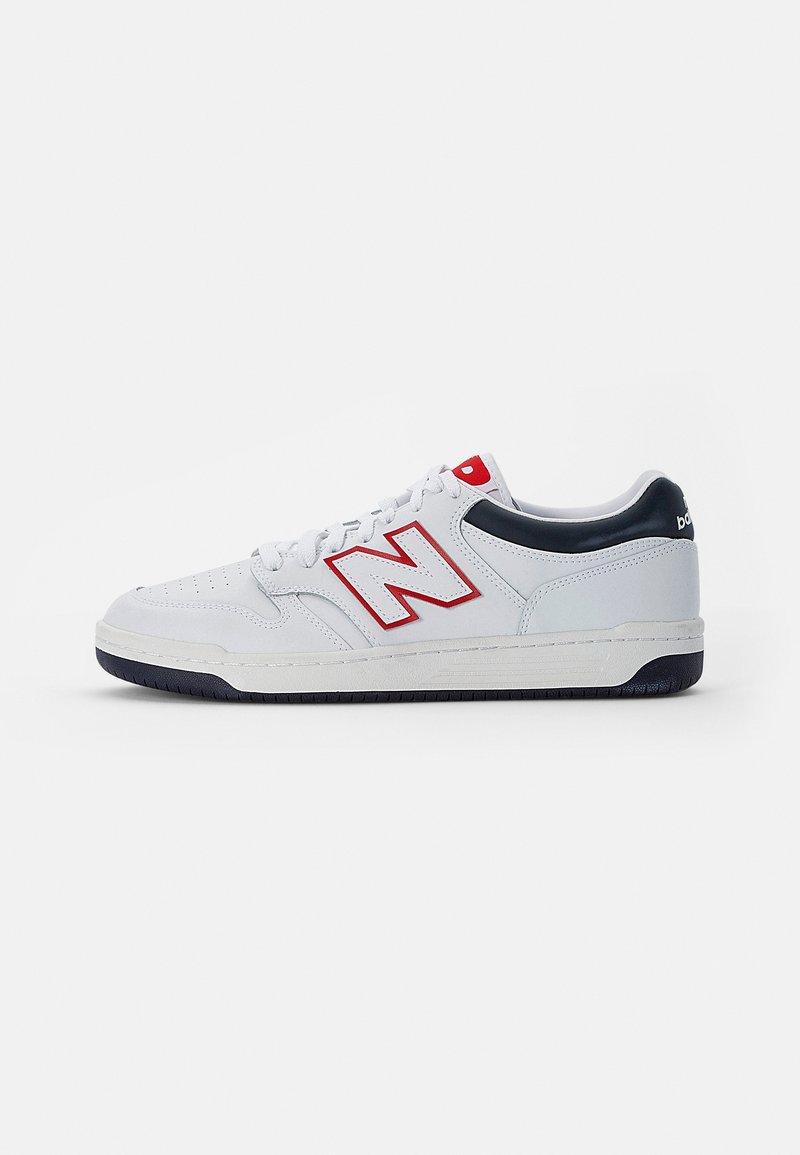 Baskets basses blanches avec des accents rouges et noirs, avec un logo "N" rouge contouré sur le côté et des détails noirs sur la semelle.