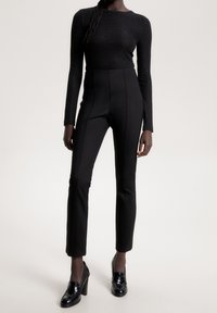 Haut noir en maille côtelée à manches longues associé à un pantalon noir taille haute ajusté avec des coutures verticales et des talons noirs pointus.