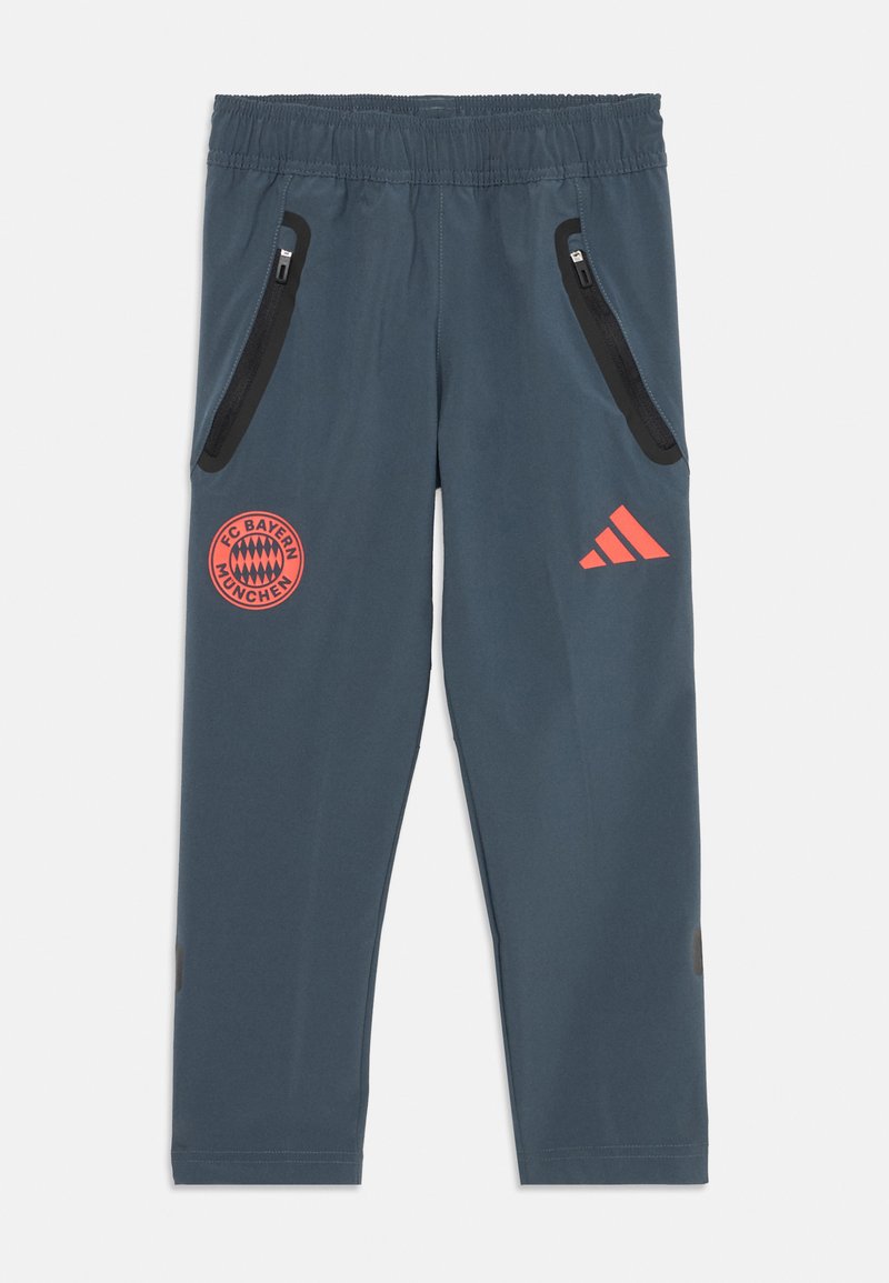 Blå treningsbukser med elastisk liv, to glidelåslommer på siden, rødt FC Bayern München-logo og oransje Adidas-detalj.