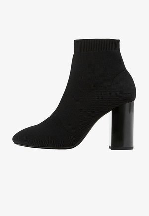 Bottine noire à cheville en tissu texturé, avec bord-côte élastique, bout pointu et talon bloc brillant.