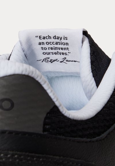 Γλώσσα παπουτσιού με μία λευκή υφασμάτινη ετικέτα που αναφέρει το απόφθεγμα, «Κάθε μέρα είναι μια ευκαιρία να επανεφεύρουμε τον εαυτό μας.» υπογεγραμμένο από τον Ralph Lauren.