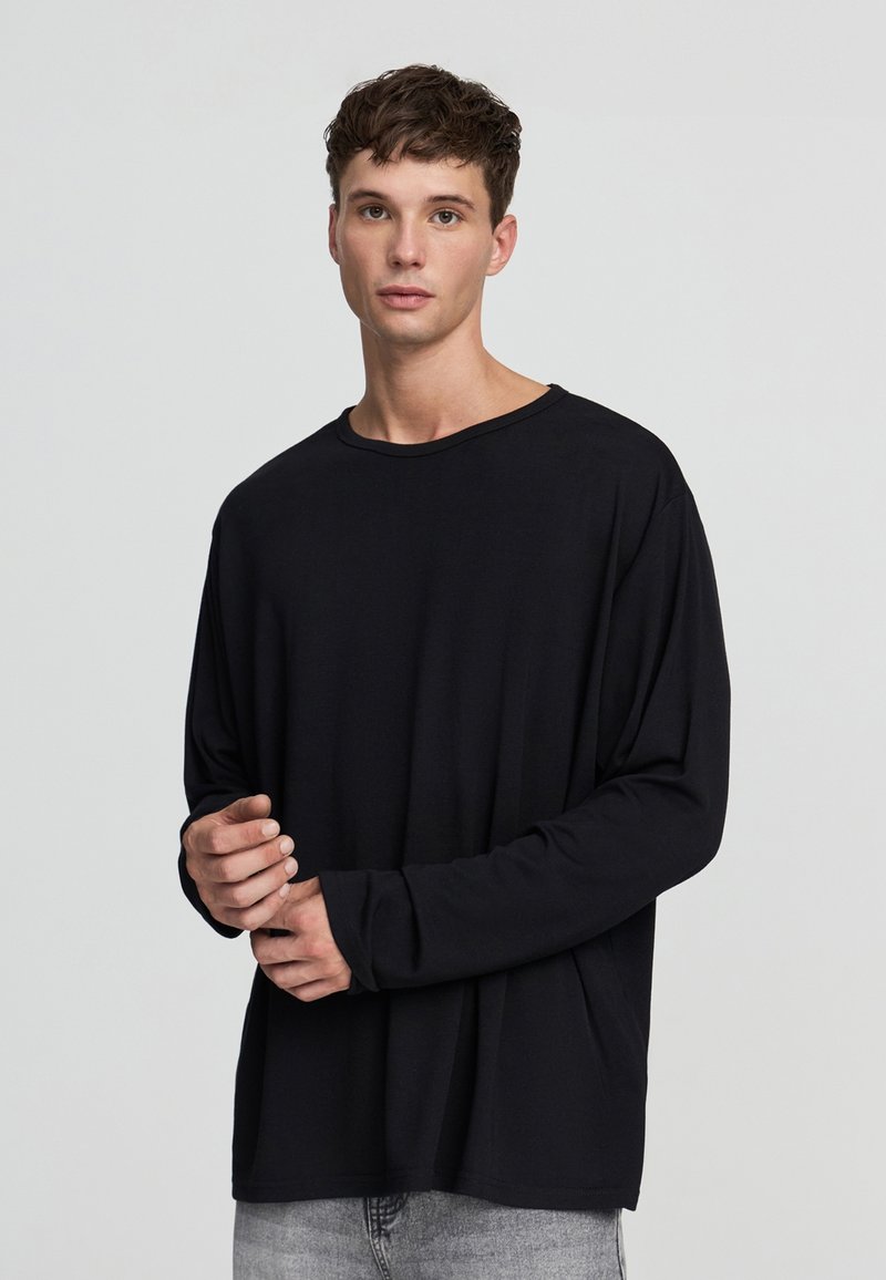 Czarna koszula z długim rękawem, uszyta z miękkiego materiału, z okrągłym dekoltem i luźnym krojem, połączona ze jasnoszarymi dżinsami.