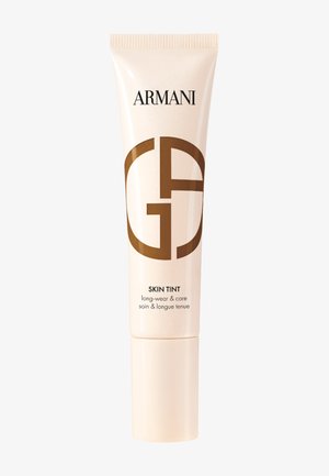 Teint Armani dans un tube beige à presser avec une finition brillante. Présente un logo marron bien en vue, étiqueté pour une tenue et un soin longue durée.
