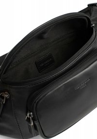 Schwarze Stofftasche mit einer externen Reißverschlusstasche, glatter Textur und einem geräumigen Innenraum. Markenetikett ist sichtbar im Inneren.