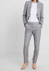 Szary garnitur w kratę o dopasowanym kroju, marynarka zapinana na jeden guzik i wąskie spodnie. Noszony na białej koszulce, w połączeniu z cielistymi szpilkami.