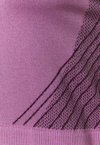 Gros plan sur un tissu tricoté lilas avec des rayures diagonales violet foncé et un ourlet côtelé en bas.