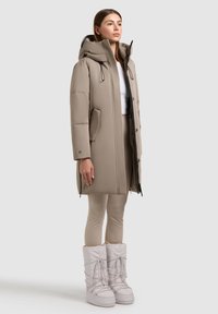 Beige padded coat with a hood, front pockets, and a zip closure. Paired with light beige leggings and white winter boots with laces.