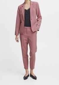 Ruusuinen räätälöity puku, jossa on yksittäinen napitus, yhdistetty mustaan pitsireunaiseen kimalleliiveihin. Mustat ballerinat täydentävät asun.