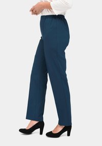 Marineblauwe elastische broek met rechte pijpen en zichtbare stiksels, gecombineerd met zwarte hoge hakken.