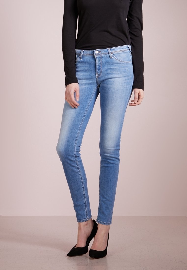 Smal jeans av ljusblå denim med blekning, klassisk femfickdesign, i kombination med en svart långärmad skjorta och svarta högklackade skor.