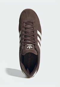 Brun mockasneaker med vita ränder, strukturerad snördesign, vadderad plös och logodetaljer på plösen och innersulan.