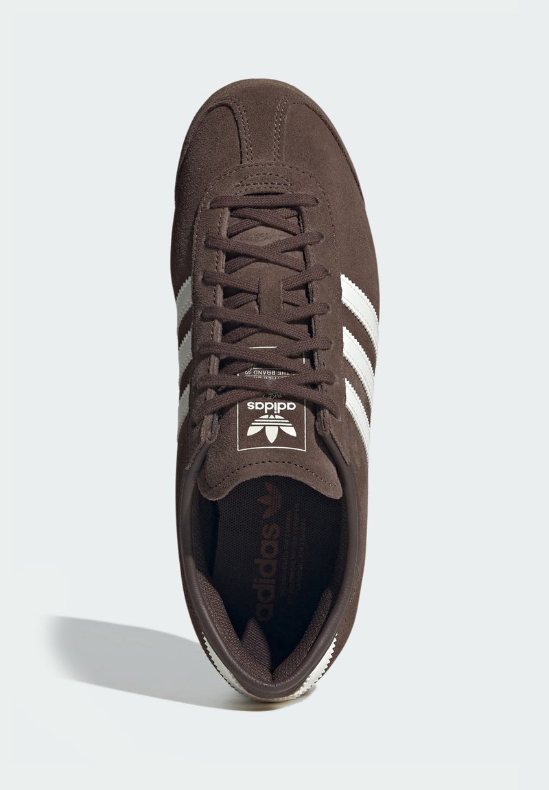 Brun mockasneaker med vita ränder, strukturerad snördesign, vadderad plös och logodetaljer på plösen och innersulan.