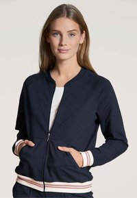 Marineblauwe zip-up jas met een ronde hals, gestreepte manchetten en zoom in lichtroze, met zijzakken en een zachte textuur.
