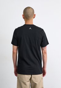 T-shirt nera con colletto tondo e maniche corte, con un piccolo logo Jumpman bianco sul retro. Tessuto di cotone morbido, vestibilità rilassata.