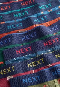 Bunt gefächerte Gummibänder mit dem Text "NEXT" in verschiedenen kontrastierenden Farben, die unterschiedliche Texturen und Muster überlagern.