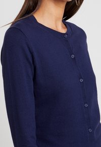 Marinblå cardigan i mjuk stickad kvalitet, med rund halsringning, knappar framtill och långa ärmar.