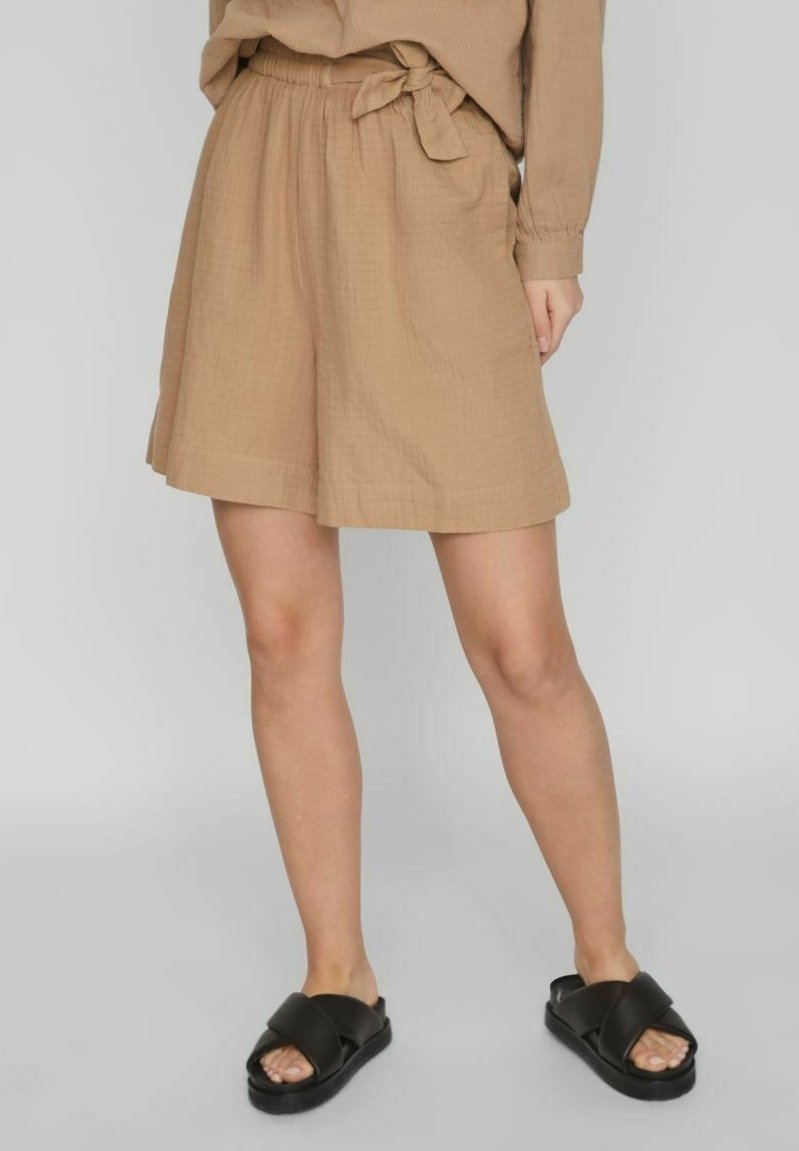 Béžové lněné šortky s elastickým pasem a bočními kapsami. Mají zavazovací detail v pase a volnější, pohodlný střih.