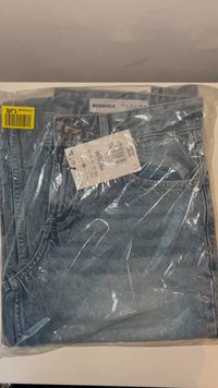 Svijetloplave traperice marke Bershka u plastičnoj ambalaži. Imaju tipični dizajn s pet džepova, metalni gumb i priloženu etiketu.