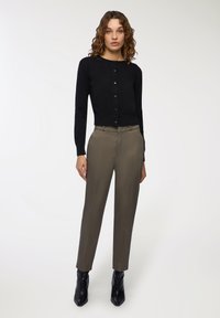 Cardigan lungo nero con maniche lunghe e bottoni, in tessuto knit leggero. Abbinato a pantaloni tagliati verde oliva e stivali neri alla caviglia.