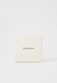 Štvorcová biela krabička značky Calvin Klein umiestnená na čistej bielej pozadí.