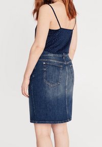 Falda lápiz de mezclilla, azul oscuro, de longitud media, con bolsillos traseros y un sutil desvanecimiento. Terminada con un dobladillo que llega justo por encima de la rodilla.