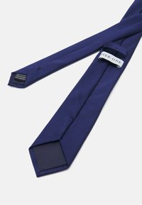 Cravate en polyester bleu marine avec une texture lisse, dotée d'une extrémité plus large et d'une étiquette avec "PIER ONE". Instruction d'entretien : nettoyage à sec uniquement.