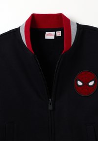 Zwarte jas met rood en grijs ribbelkraag, rits aan de voorkant en geborduurd Spider-Man embleem op de borst. Zacht materiaal, ontworpen voor kinderen.