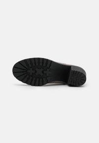 Suela de goma negra con un patrón de tracción, diseñada para ofrecer agarre. El material superior en gris es suave y complementado por un tacón robusto.