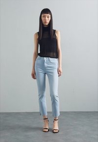 Svart gjennomsiktig ermeløs topp, lyseblå tettsittende jeans med ankellengde, og svarte stroppehæler. Enkelt design, glatt tekstur.