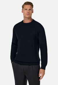 Marine blauwe geribde gebreide trui met lange mouwen, ronde hals en textuurstof. Gecombineerd met donkere broeken, wat een fitted silhouet toont.