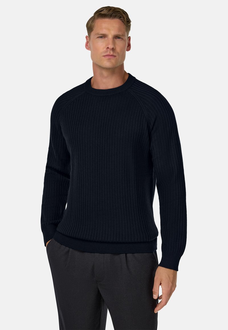 Marine blauwe geribde gebreide trui met lange mouwen, ronde hals en textuurstof. Gecombineerd met donkere broeken, wat een fitted silhouet toont.