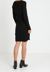 Abito nero lavorato a maglia con maniche lunghe e orlo arrotondato. Presenta un motivo testurizzato sulle spalle, abbinato a stivaletti lucidi fino alla caviglia.