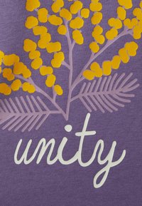 Fioletowa tkanina z kwiatowym wzorem przedstawiającym żółte kwiaty i brązowe liście. Słowo "jedność" jest wyraźnie napisane białym pismem odręcznym.