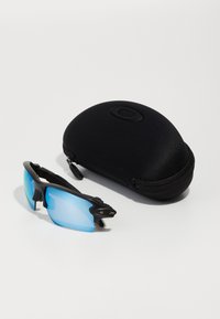 Gafas de sol deportivas negras con lentes azules, colocadas junto a un estuche rígido negro, que presenta un diseño redondeado y un cierre de cremallera.