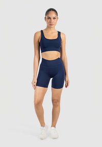 Marinblå sportset med en kort ärmlös topp och höga midjebyxor. Tillverkad av stretchigt tyg, har sömlös design och minimal märkning.