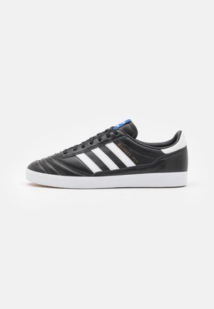 Schwarze synthetische Sneaker mit drei weißen Streifen, einer strukturierten Zehenkappe und einer weißen Gummisohle. Blaue Akzentfarbe auf der Zunge. Text lautet "Gazelle WTR."