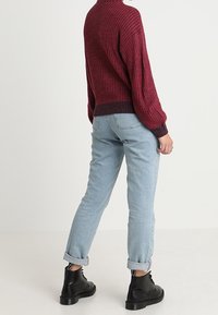 Maglione bordeaux a coste con colletto alto, abbinato a jeans azzurri risvoltati e stivaletti neri con lacci. Il tessuto appare testurizzato e accogliente.