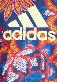 Multibarevná bavlněná košile s květinovým vzorem v růžové, oranžové a modré barvě, s výrazným žlutým logem Adidas na přední straně.