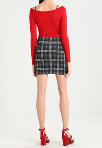 Rotes Langarmoberteil mit schulterfreier Gestaltung, kombiniert mit einem schwarz-weiß karierten Minirock. Rote Sandalen mit dickem Absatz vervollständigen das Outfit.