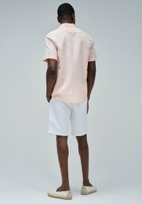 Camisa de manga corta rosa claro, pantalones cortos blancos y alpargatas beige. La camisa cuenta con un cuello abotonado y un corte holgado.