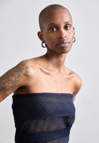 Top senza spalline di colore navy in tessuto testurizzato, con ritagli in rete orizzontali. Il modello ha la testa rasata e tatuaggi ben visibili sulla spalla.